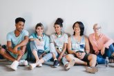 Glad students wearing stylish sneakers and accessories sitting together on the floor with legs crossed. Excited young people of different nationalities relaxing in light room and laughing.. Glad students wearing stylish sneakers and accessories sitting together on the floor with legs crossed. Excited young people of different nationalities relaxing in light room and laughing..