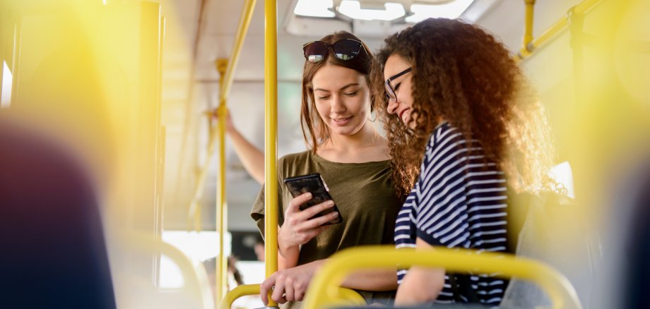 Zwei Freundinnen stehen im Bus und unterhalten sich.