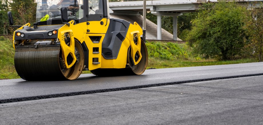 Eine Asphaltwalze verdichtet auf einer Baustelle frischen Heißasphalt auf der Fahrbahn.