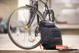 Auf dem Bild zu sehen ist ein Rucksack, der an ein Vorderrad eines Fahrrades gelehnt ist.