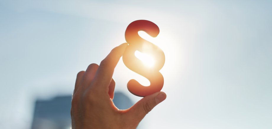 Hand hält Paragraphen Symbol in Sonne