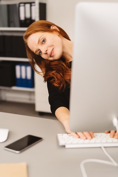 Playful businesswoman peering around her monitor Playful businesswoman peering around her monitor