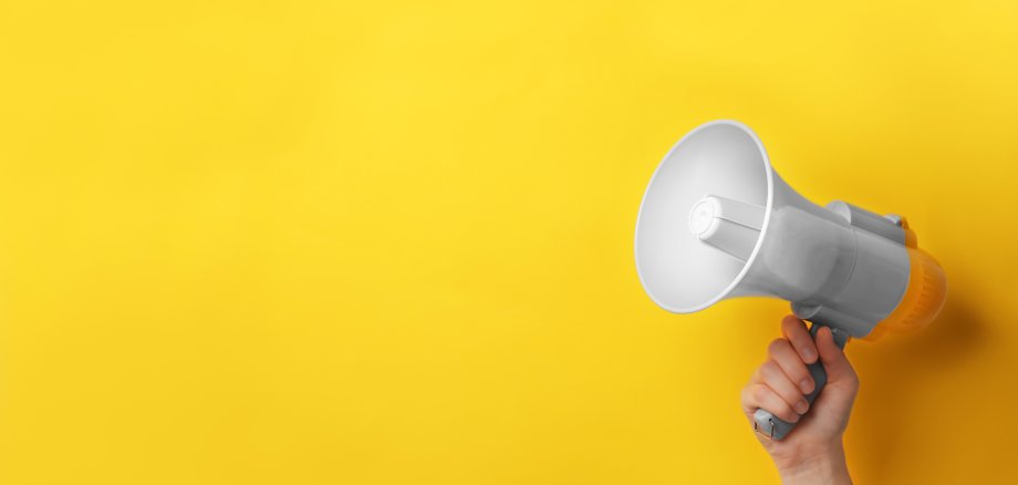 Mann hält Megaphon vor gelben Hintergrund