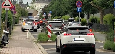 Zu sehen ist ein Foto der aktuellen Situation in der Zeppelinstraße mit einigen Autos, die teilweise auch über den Gehweg fahren.