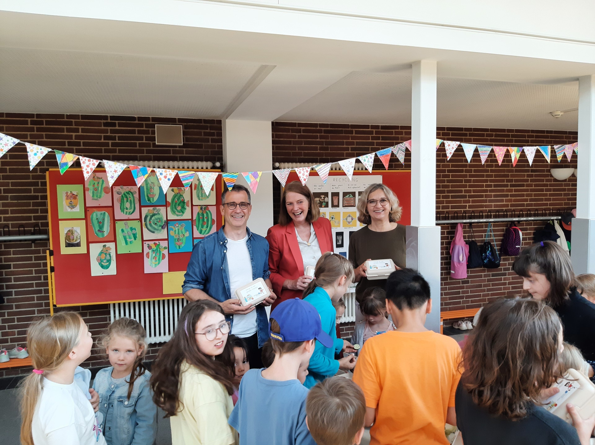 Alan Moss, Antje Runge und Andrea Königslehner verteilen die beliebten Stadtwerke Oberursel-Snackboxen an die Erstklässlerinnen und Erstklässler der Grundschule Weißkirchen.