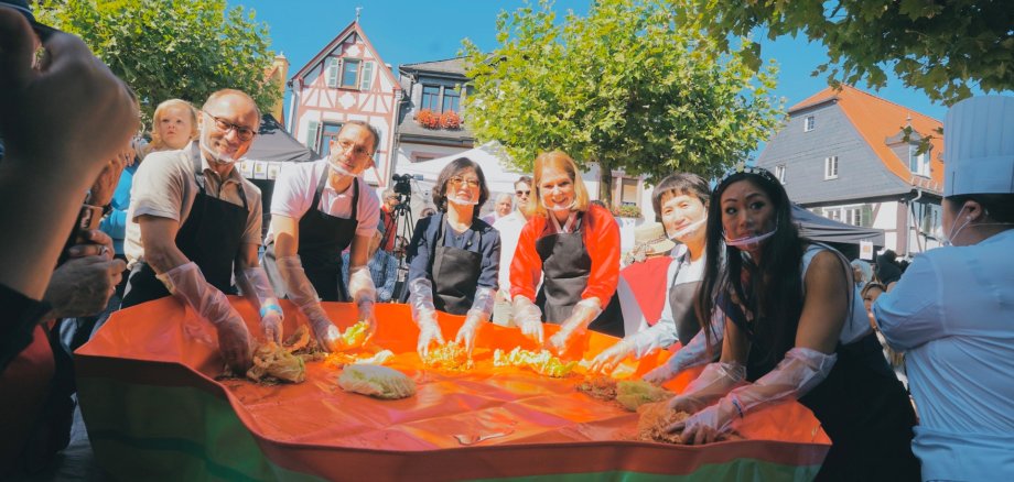 Zu sehen sind bei der Zubereitung des südkoreanischen Nationalgerichts Kimchi v.l.n.r. Stadtverordnetenvorsteher Lothar Köhler, Erster Stadtrat Jens Uhlig, Generalkonsulin Eunjeong Kim der Republik Korea in Frankfurt am Main, Bürgermeisterin Antje Runge, Abteilungsleiterin für Soziales und Bildung in Ulsan Nam-gu Jang Eun Lyeong und die aktuelle Brunnenkönigin Tanja Scherer.