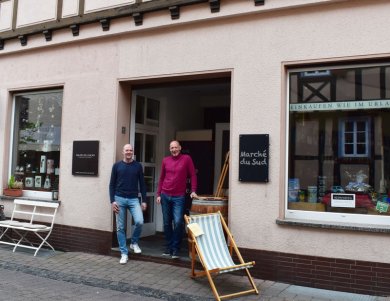 Bild: Heutiges Haus. Fenster und Türen sind ähnlich. Vor der Tür stehen die Inhaber der beiden Geschäfte.