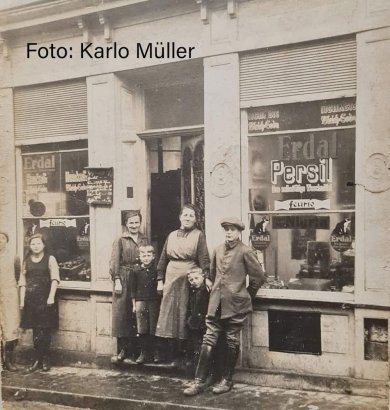 Blick auf den ehemaligen Kolonialwarenladen in der Ackergasse 28. Davor stehen mehrere Personen und Kinder