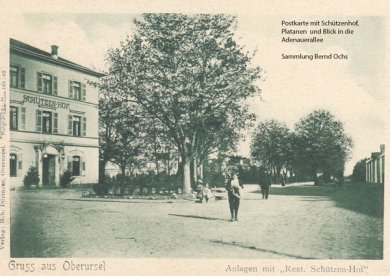 Postkartenansicht aus der Sammlung von Bernd Ochs. Zu sehen ist das alte Gasthaus Zum Schützenhof. Es stand an der Bärenkreuzung. Dort wo heute der Rossmann und die Post ist. Der Schützenhof war von Platanen umgeben. Eine steht noch heute an der Fußgängerampel. Auf der Postkarte blickt man auf die Platane und die Adenauerallee hinunter. Hier stehen noch keine Häuser.