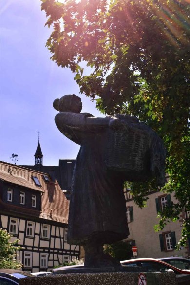 Skulptur des Wäschfraa-Brunnens: Eine Frau mit Dutt trägt eine Wäschekorb vor sich her