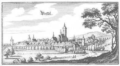 Historische Stadtansicht. Wenige Häuser sind von einer Stadtmauer umgeben. An manchen Stellen steht ein alter Stadtmauer-Turm. Entlang der Stadtmauer stehen Bäume.